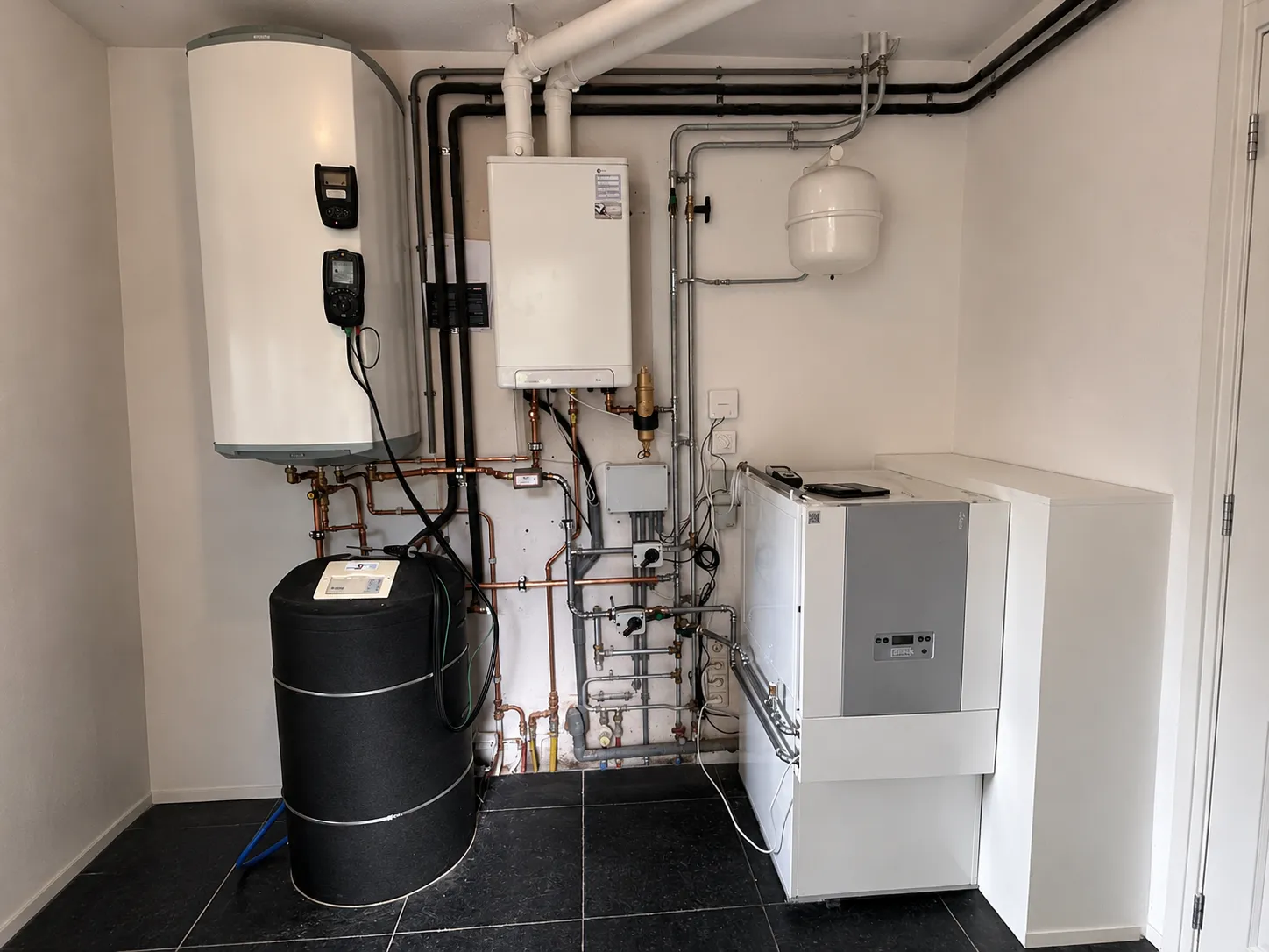 Technische ruimte met nieuwe cv-ketel en heteluchtverwarming naast een bestaande zonneboilerinstallatie